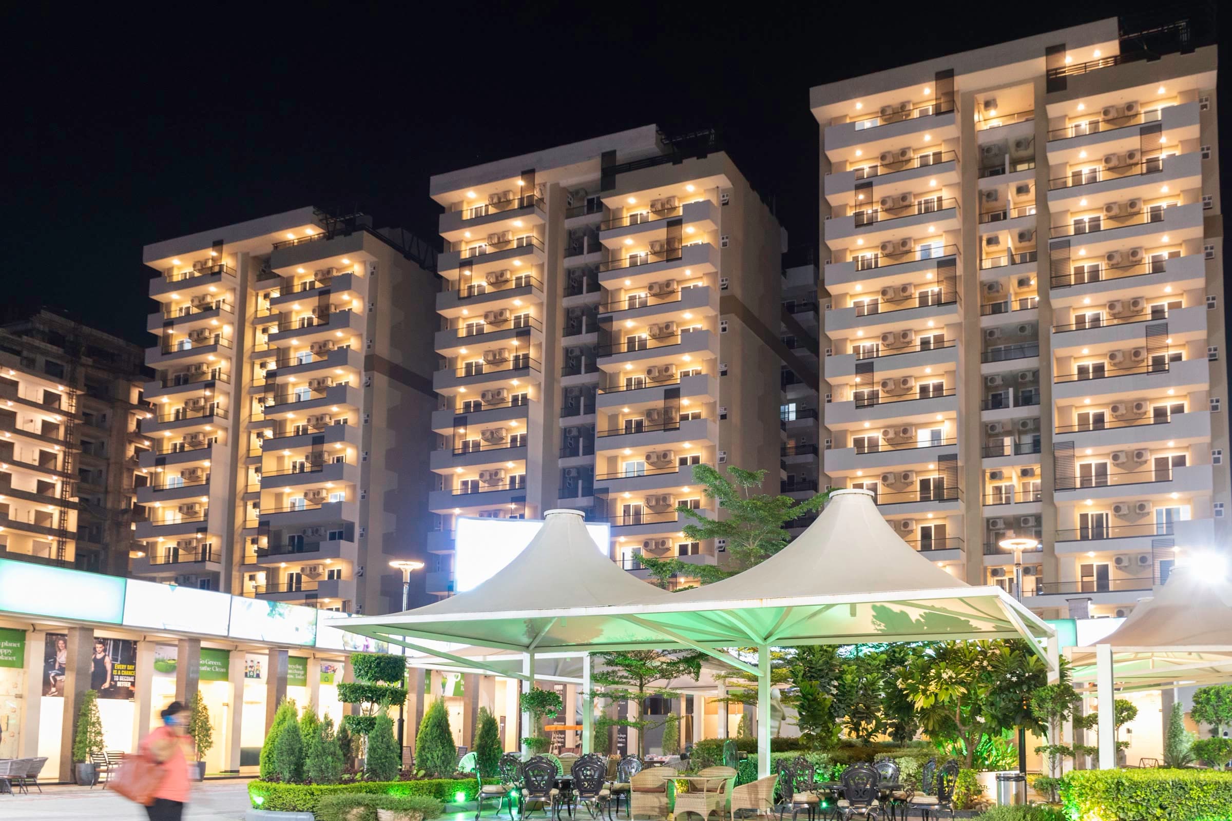 Landscaped courtyard lit at night beneath residential towers in Zirakpur